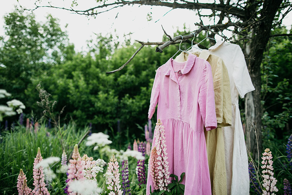 Natural colored dresses hanging on on a tree in the garden with lupine flowers. Concept organic clothes, eco-friendly, ecological fashion